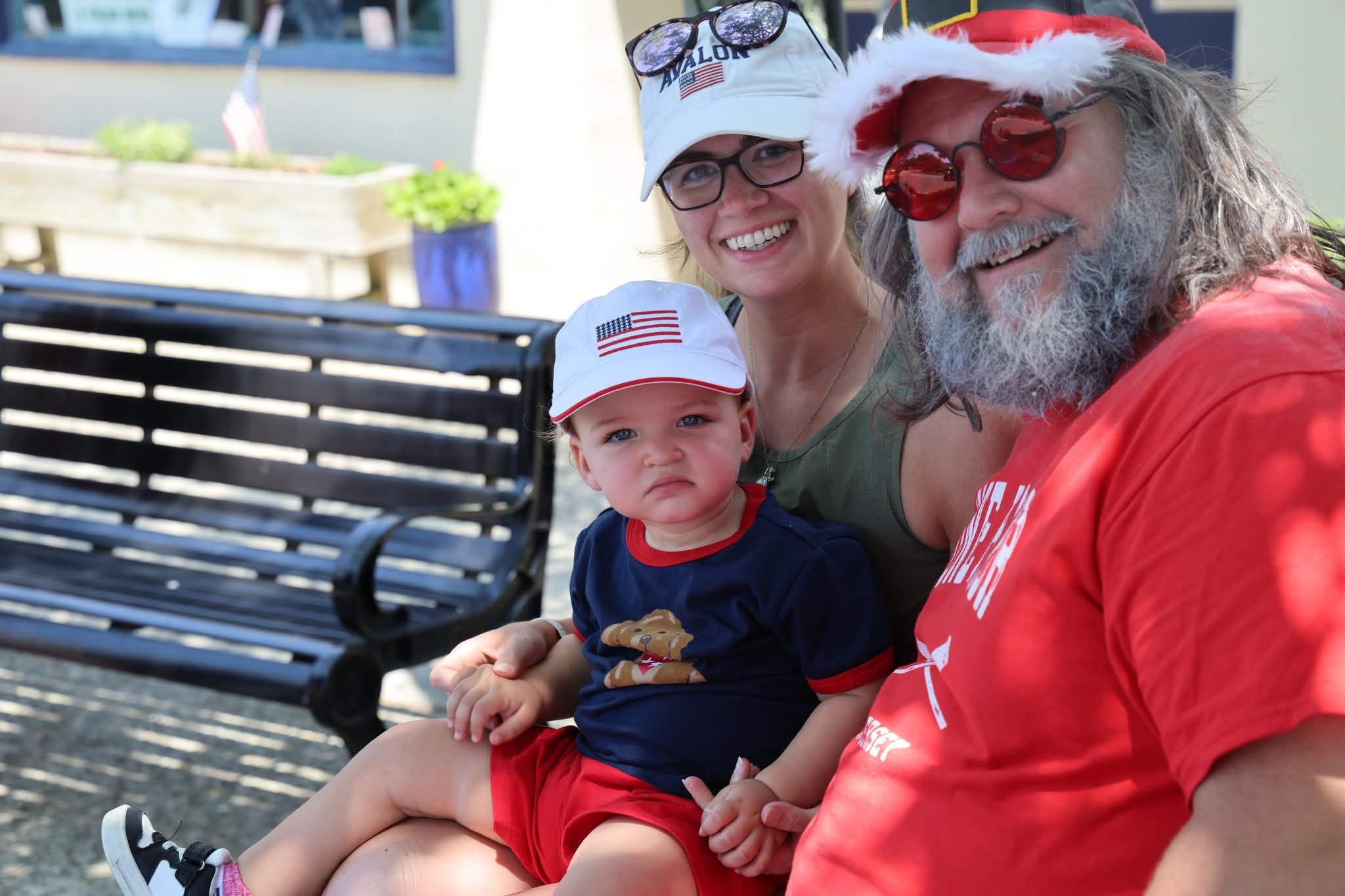 Cape May County Santa with a young mom in an Avalon hat and her baby in an American flag hat on a bench