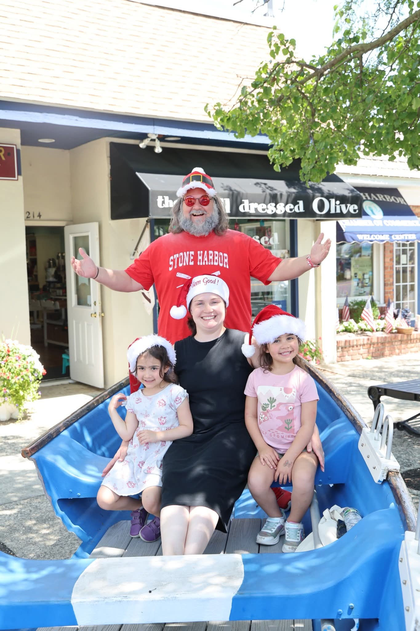 Cape May County Santa with arms wide open behind a mom and two girls in Santa hats in the Stone Harbor boat