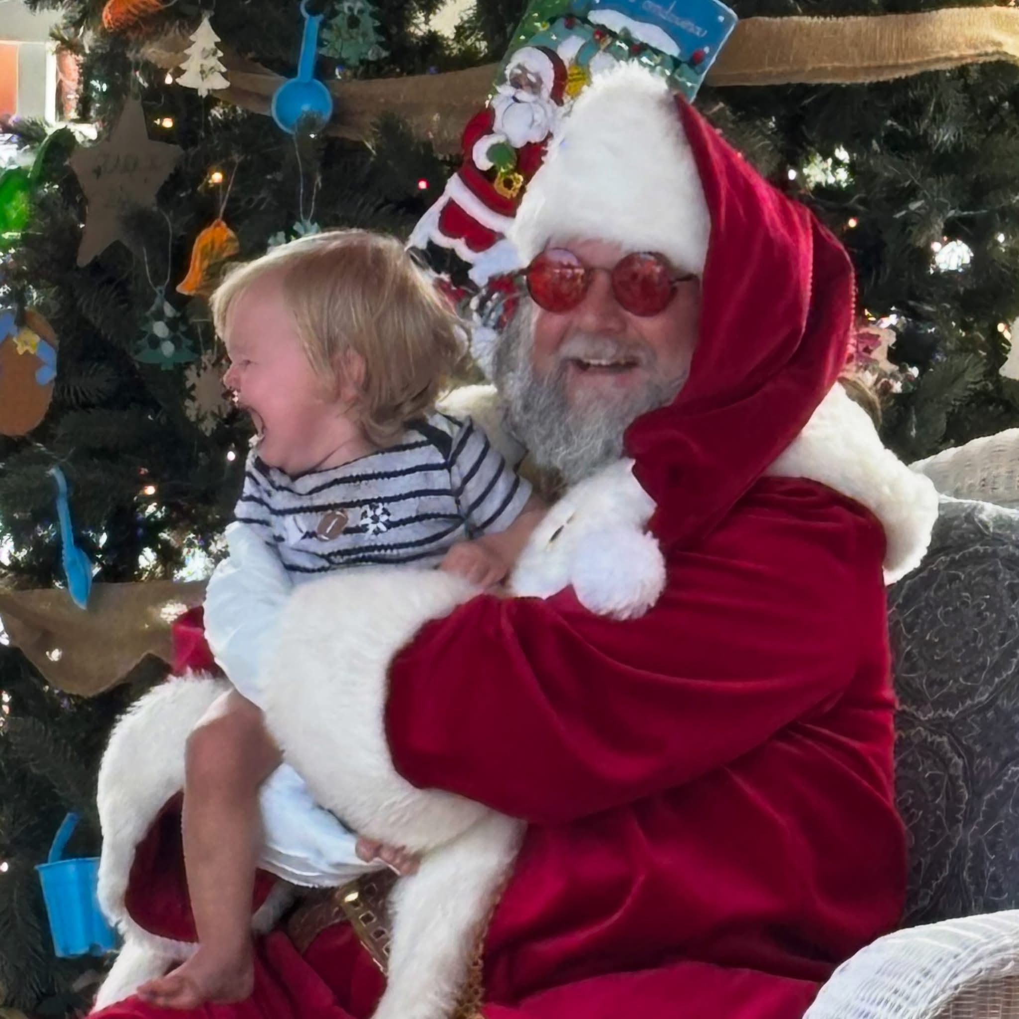 Cape May County Santa holding a crying toddler in front of a decorated Christmas tree indoors