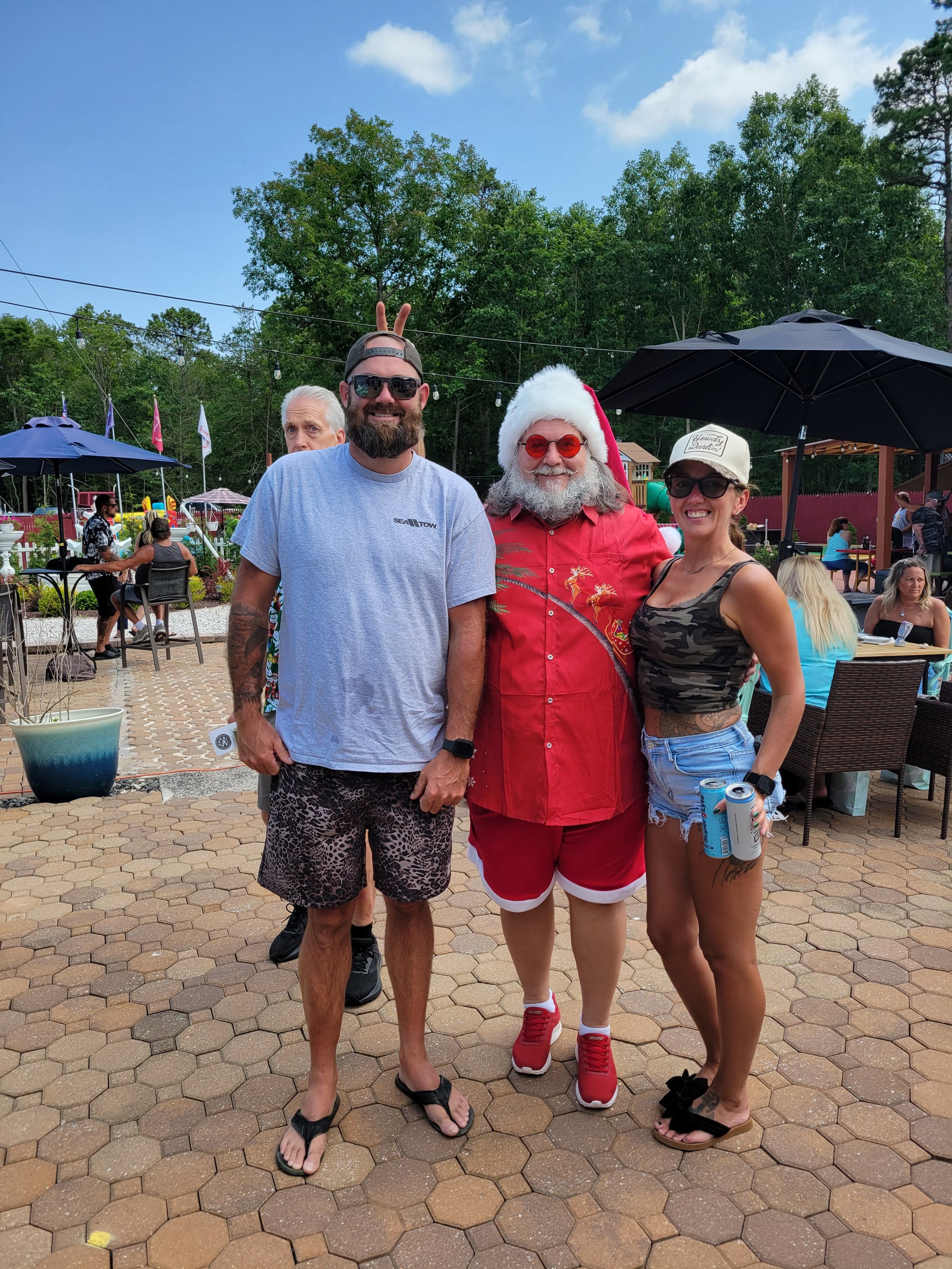 Cape May County Santa in Hawaiian shirt posing with a couple at an outdoor patio venue