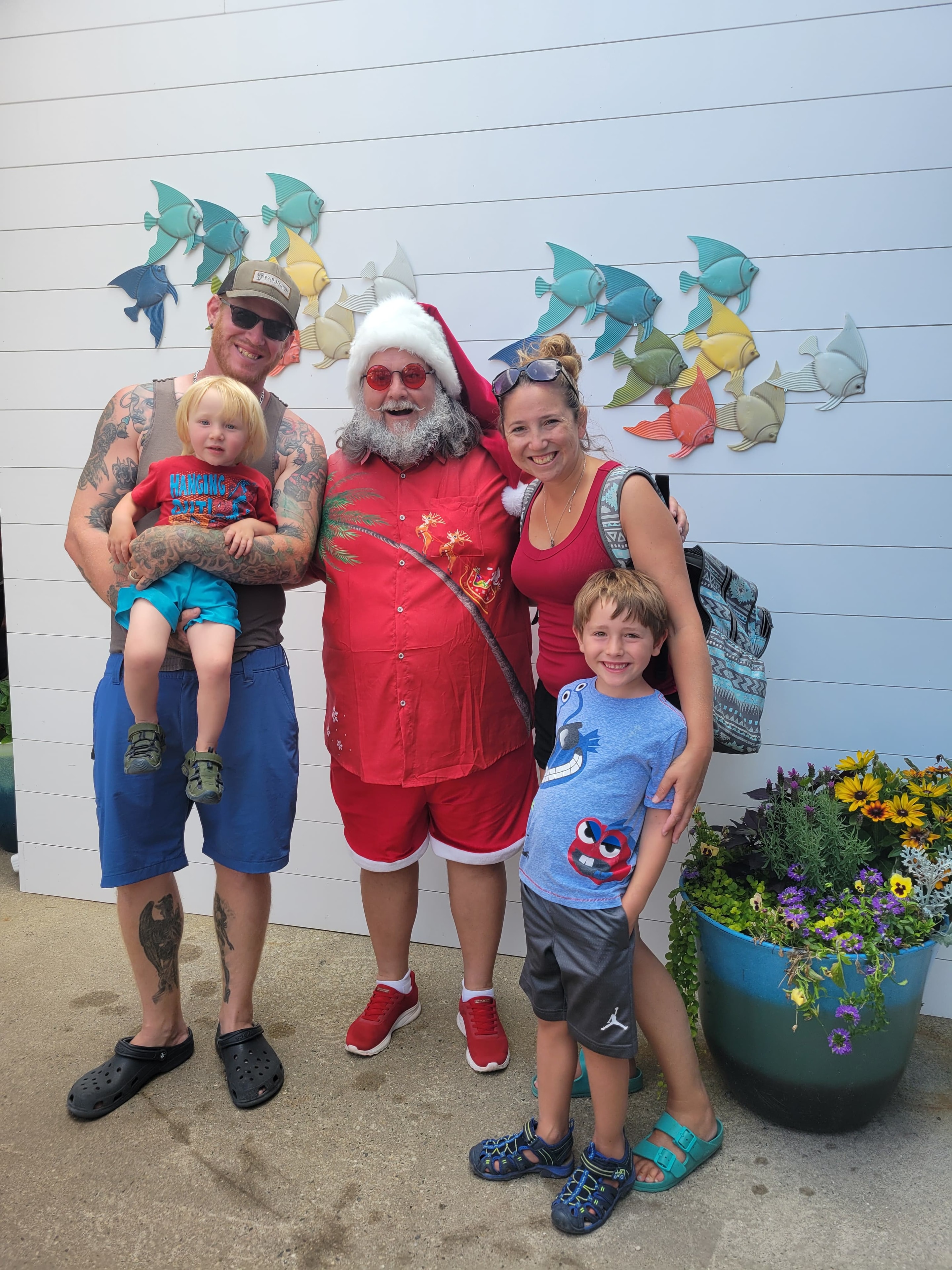 Family posing with Cape May County Santa in front of a colorful fish mural wall