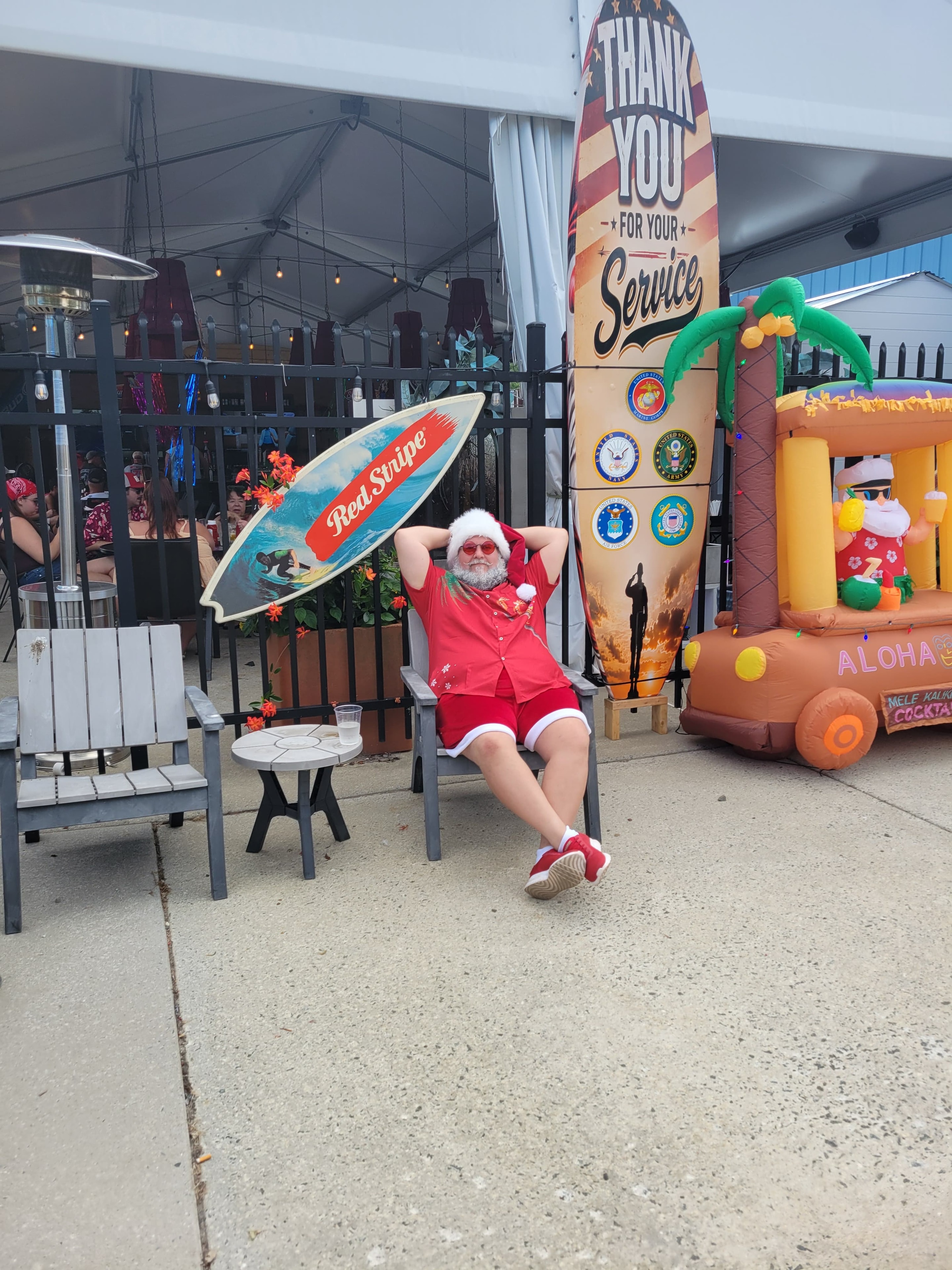 Cape May County Santa relaxing in an Adirondack chair beside a Thank You For Your Service surfboard display