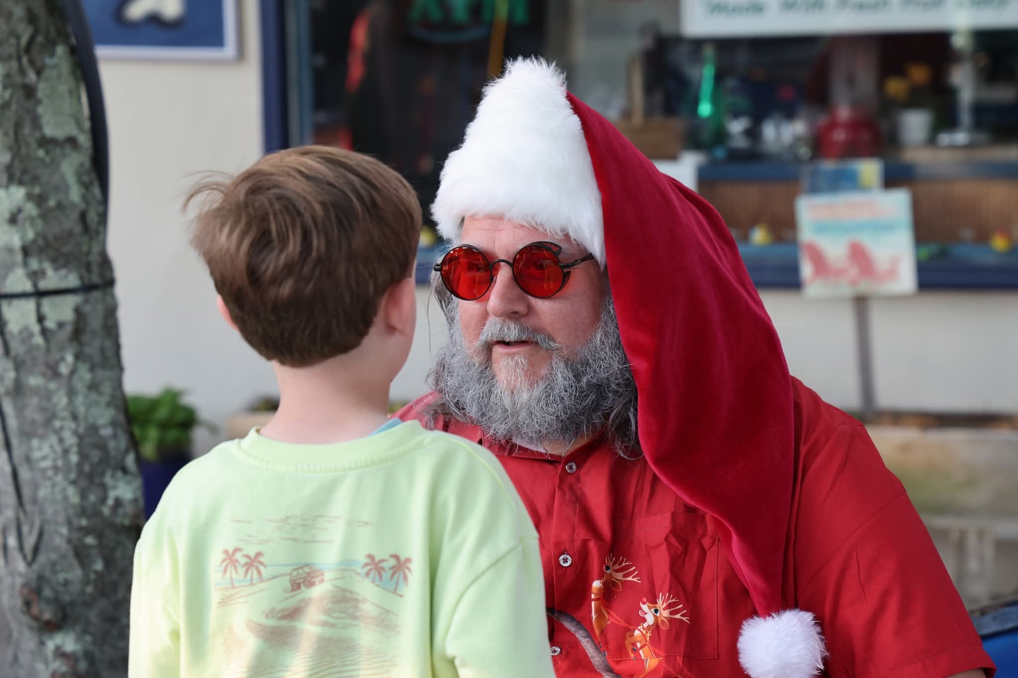 Cape May County Santa leaning in close talking to a boy in a green palm tree shirt
