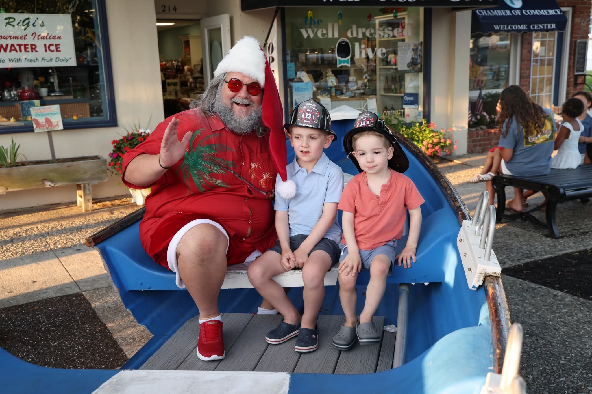 Cape May County Santa waving with two little boys wearing firefighter helmets in the Stone Harbor boat