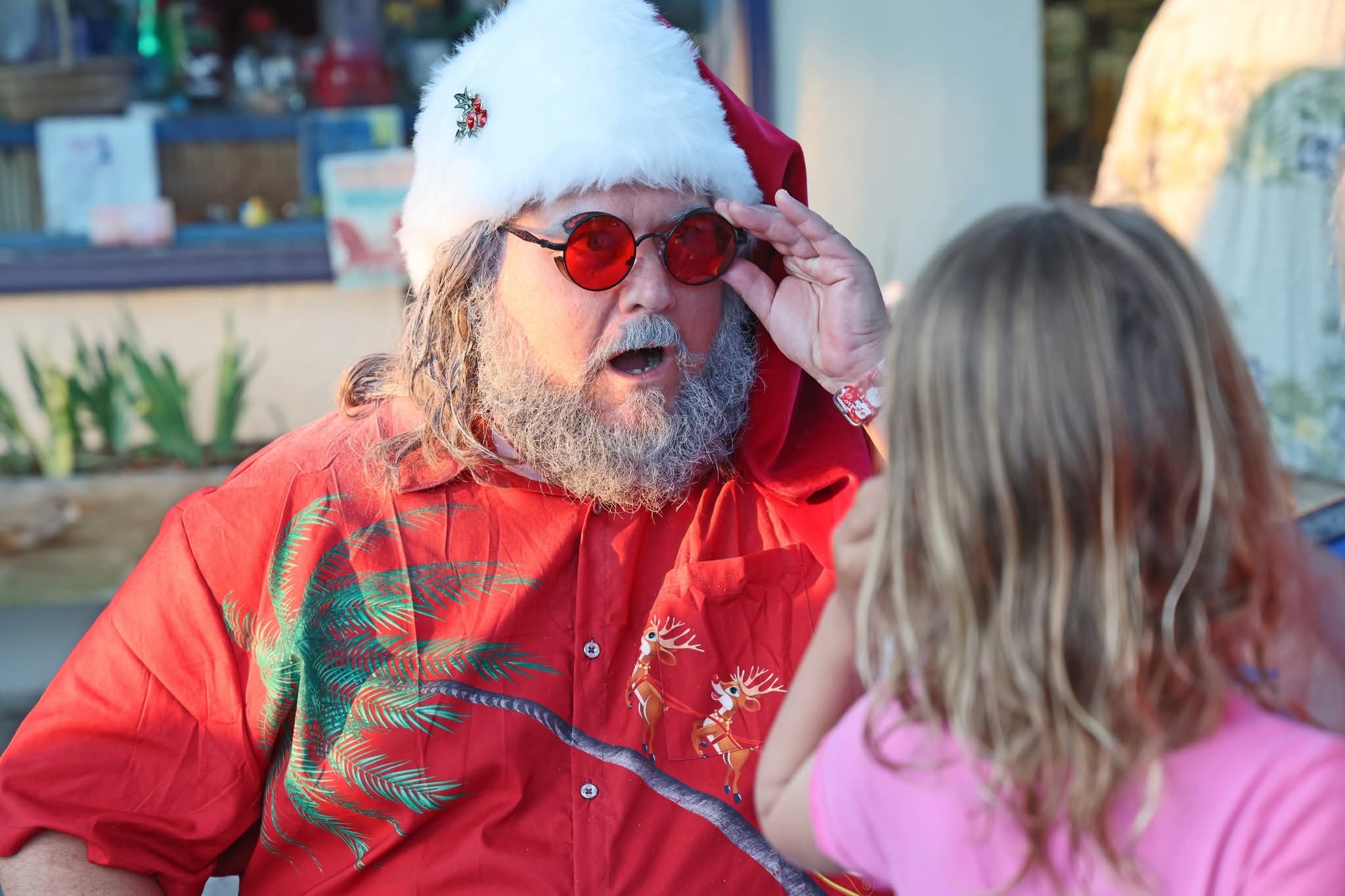 Cape May County Santa peering over his red sunglasses at a little girl