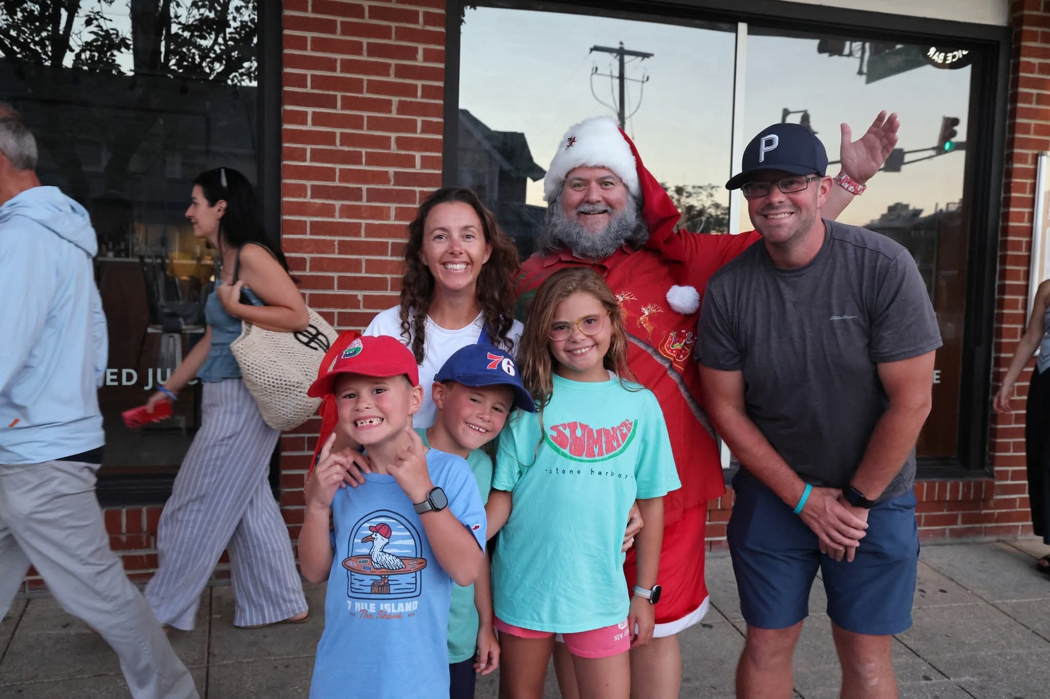 Cape May County Santa with a family of five in front of a brick storefront, dad waving