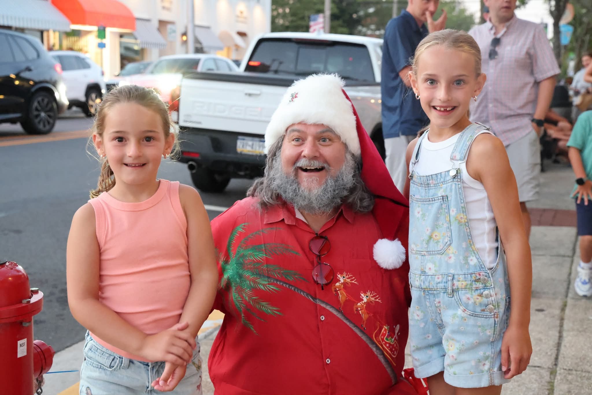 Cape May County Santa leaning in with a huge smile between two girls on the street