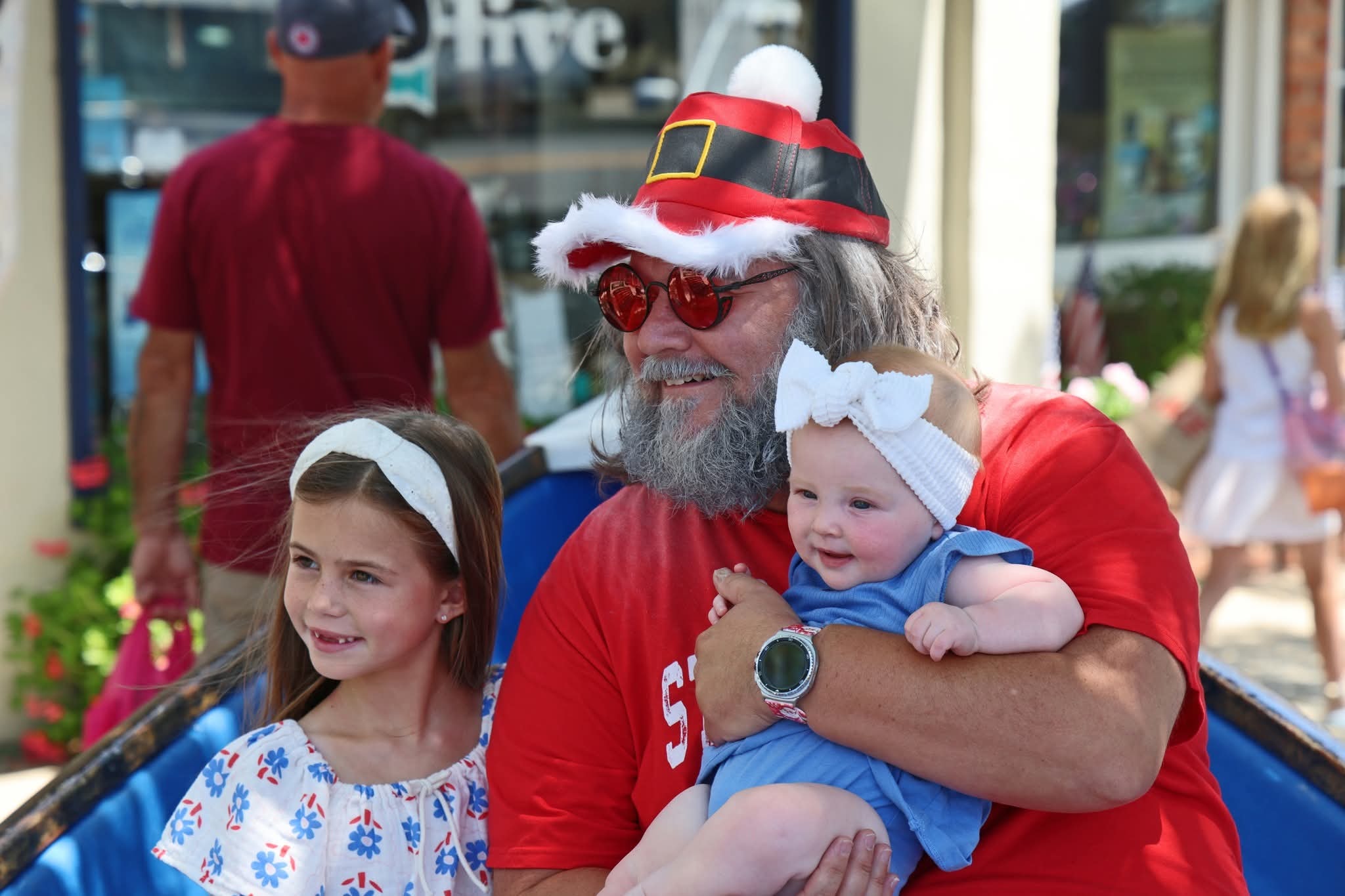 Cape May County Santa holding a baby girl with a white bow next to a young girl in the Stone Harbor boat